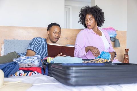 African american couple packing suitcase while reading travel journal on bed