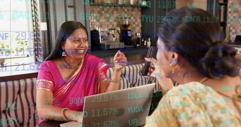Indian woman in pink saree smiling and gesturing at laptop during cafe meeting