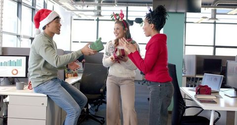 Multicultural coworkers celebrating holiday by exchanging gifts in modern open-plan office