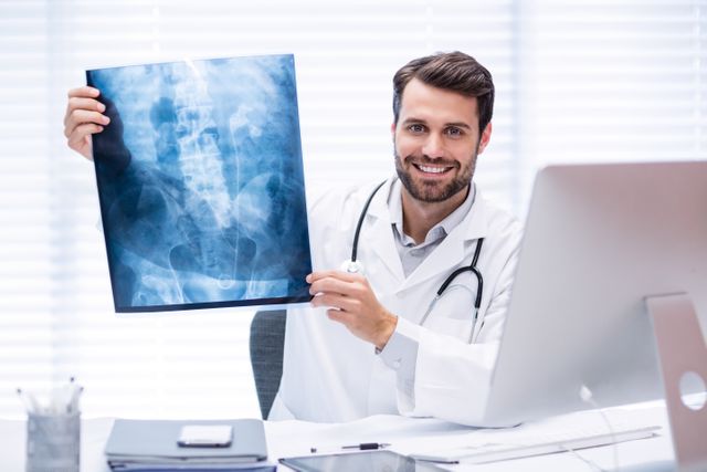 Male doctor holding and examining an x-ray in a modern clinic. He is smiling and appears confident. Ideal for use in healthcare, medical, and professional settings to depict medical expertise, patient care, and diagnostic processes.