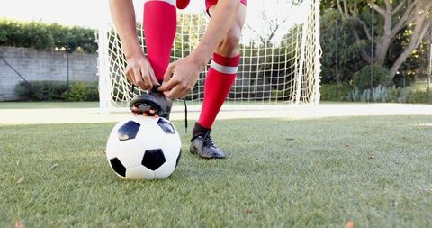 Teen Football Player Lacing Cleat on Soccer Field