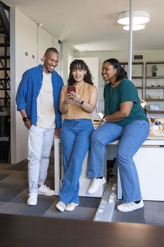Sharing smartphone screen in modern open-plan office, diverse coworkers collaborating