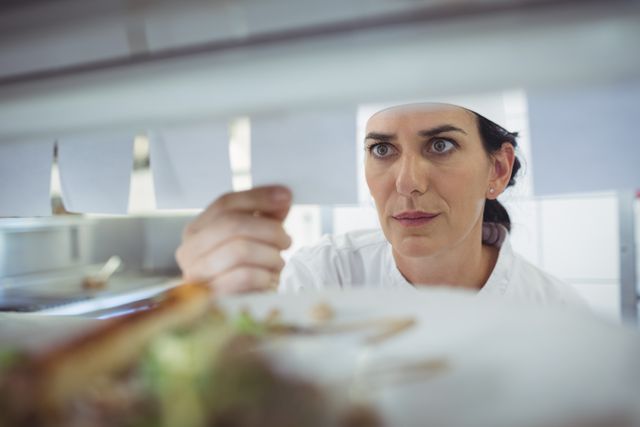 Female chef in a commercial kitchen attentively checking an order list. Ideal for use in articles or advertisements related to the restaurant industry, culinary arts, professional cooking, and kitchen management.