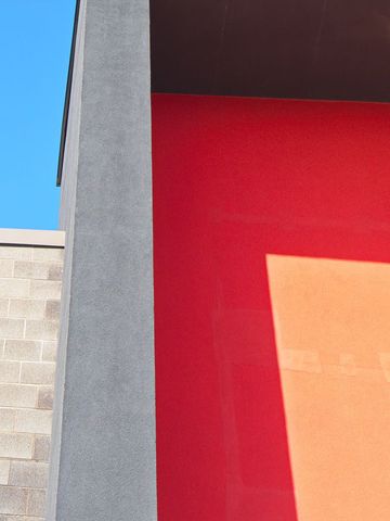 Minimalist architectural composition bold red wall gray column blue sky and orange shadow
