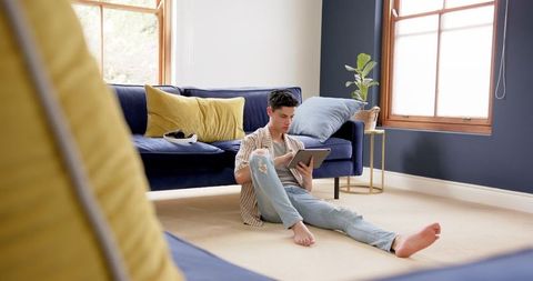 Young Man Relaxing on Floor Using Tablet in Modern Living Room