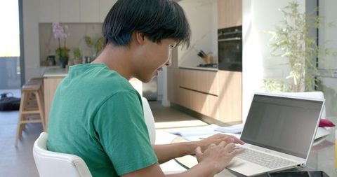 Young Asian Man Typing on Laptop at Home in Modern Kitchen