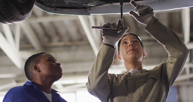 Image of two diverse female car mechanics repairing car. working in car repair shop and running small feminine business concept.