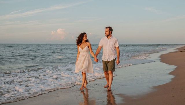 Romantic couple walking hand in hand along golden shoreline at sunset barefoot