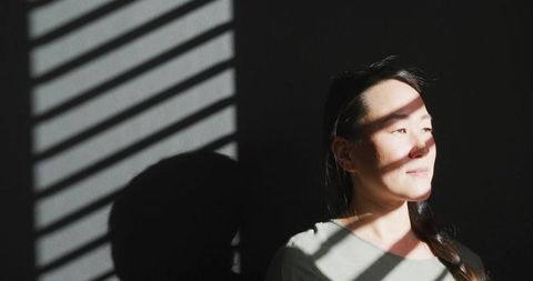Korean woman standing in dramatic blind stripe light, contemplative high-contrast portrait