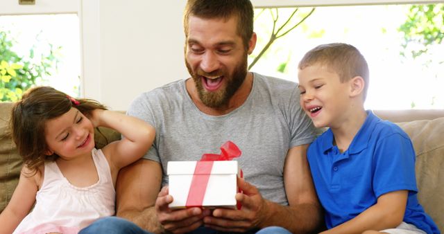 Happy Father Receiving Gift from Excited Children on Couch - Download Free Stock Images Pikwizard.com