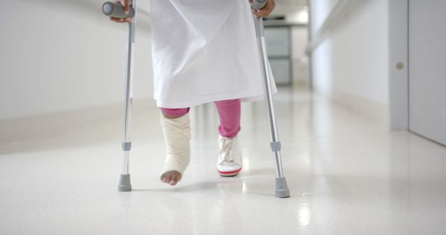 Child using crutches walking down hospital corridor. Ideal for medical training, healthcare promotion, rehabilitation programs, and injury recovery topics.