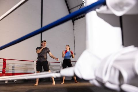Boxing coach training female athlete in ring with red hand wraps and focused stance