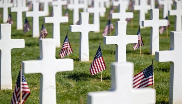 Sunlit rows of white marble cross grave markers with american flags for memorial tribute
