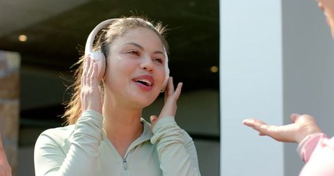 Young woman enjoying music on wireless headphones while chatting with friend on sunlit patio