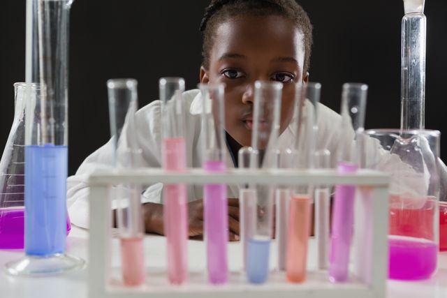 Young schoolgirl attentively observing colorful chemical reactions in test tubes. Ideal for educational content, science-related articles, STEM promotion, and children's learning materials.