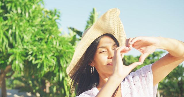 Young Woman in Straw Hat Making Heart Shape with Hands in Tropical Setting - Download Free Stock Images Pikwizard.com