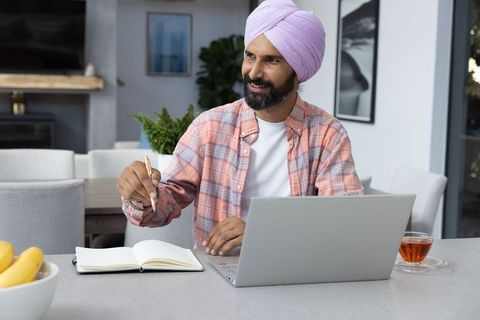Man in lavender turban writing at modern home workspace