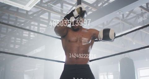 Leaning muscular boxer resting on top rope in backlit hazy gym, gloves raised, gritty determination