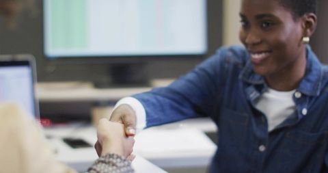 Smiling businesswoman shaking hands at modern office desk during professional meeting