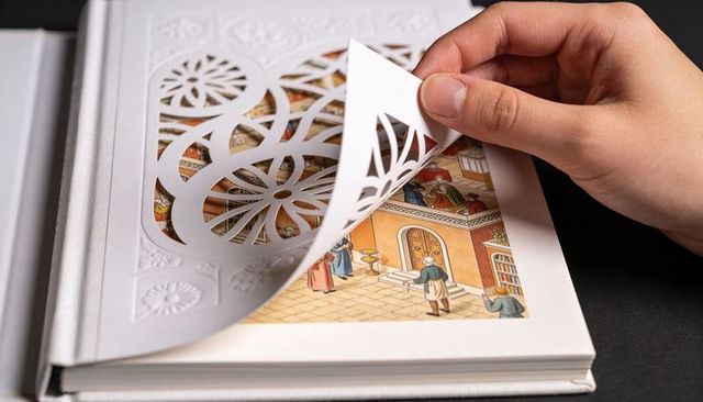 Hand lifting die-cut embossed page revealing miniature courtyard illustration