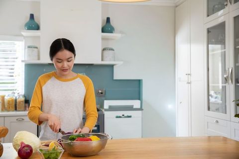 Asian woman preparing colorful vegetables on wooden island in modern minimalist kitchen