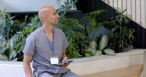 African american nurse sitting in modern hospital lobby holding tablet and smiling