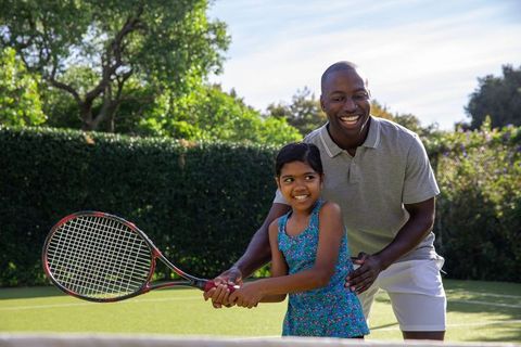 Father Guiding Child on Backyard Tennis Court with Embrace of Fun Coaching