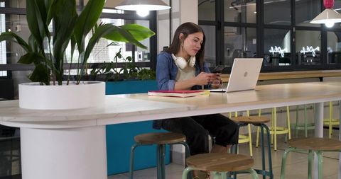 African american woman working remotely in modern coworking space with laptop and phone