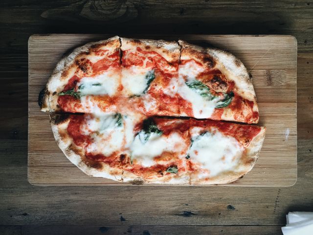 Freshly baked Margherita pizza with cheese and basil on wooden board viewed from above. Ideal visual for food blogs, restaurant menus, pizzeria promotions, and culinary magazines emphasizing traditional Italian cuisine.