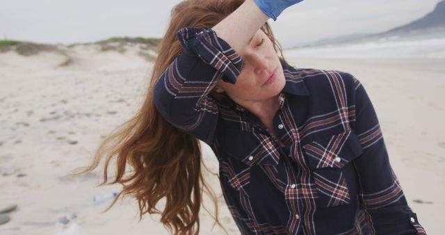 Caucasian woman wearing latex glove rubbing forehead looking toward sea and smiling. ecology beach conservation volunteer.