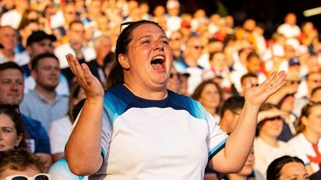 Passionate woman cheering and raising hands in sunlit stadium crowd