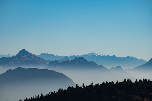 Beautiful view of mountain ranges covered in morning fog under a clear blue sky. Ideal for use in travel and nature blogs, environmental campaigns, desktop wallpapers, and inspirational posters showcasing serenity and natural beauty.