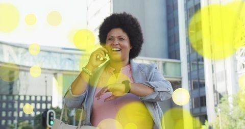 Smiling businesswoman talking on phone while checking smartwatch in modern city street