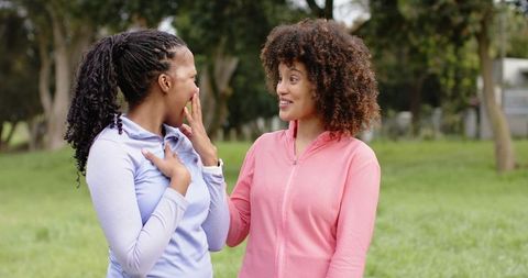 Diverse female friends laughing and reacting while chatting in park wearing zip-up jackets