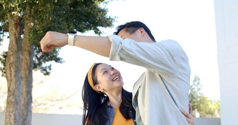 Young asian couple celebrating new car holding key fob outdoors in sunlight