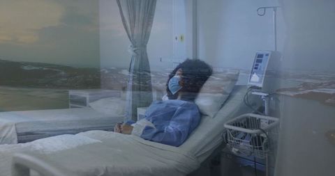 Patient lying in hospital bed wearing mask and gown with iv pump, monitor and seascape reflection