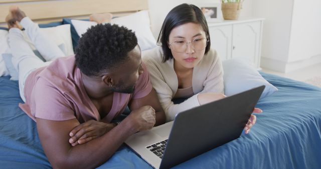 Happy diverse couple using laptop and lying in bedroom - Download Free Stock Photos Pikwizard.com