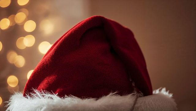 Resting red Santa hat with white faux-fur trim and warm bokeh fairy lights backdrop