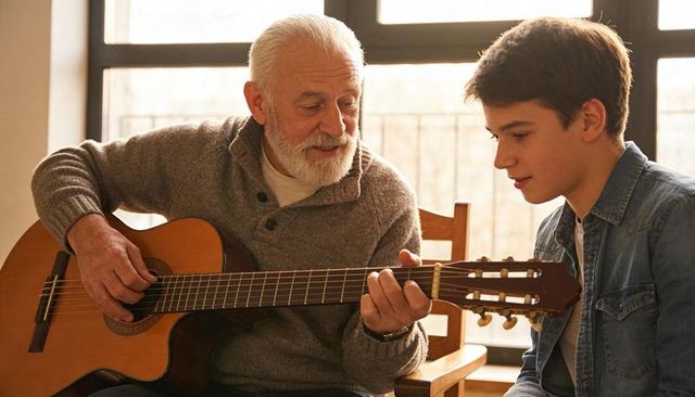 Senior man teaching teen acoustic guitar in sunlit home family music lesson