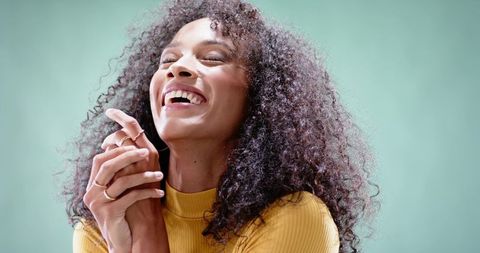 Radiant laughing woman with voluminous curly hair wearing mustard turtleneck and gold rings
