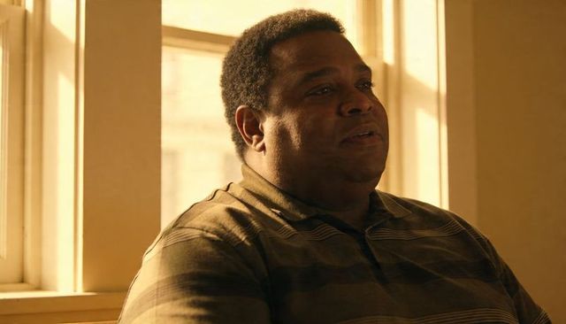 Contemplative man sitting by sunlit window looking thoughtful wearing brown striped polo