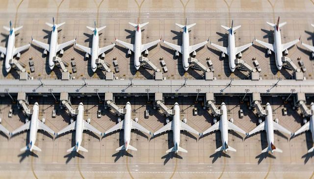 Aerial view showing rows of commercial airliners parked at airport gates with jet bridges