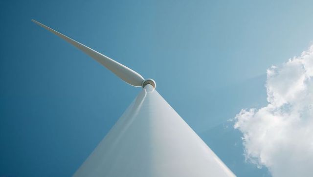 Towering wind turbine rising into blue sky with single blade and cumulus cloud