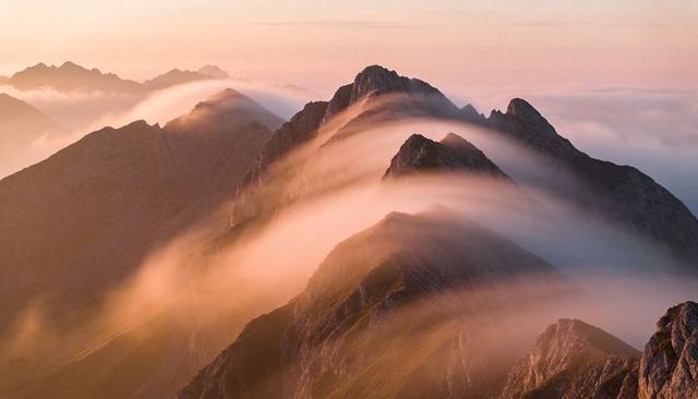 Sunlit mist cascading over jagged alpine ridge during golden hour