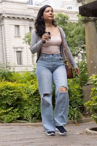 Young woman walking through urban courtyard carrying takeaway coffee and leather bag