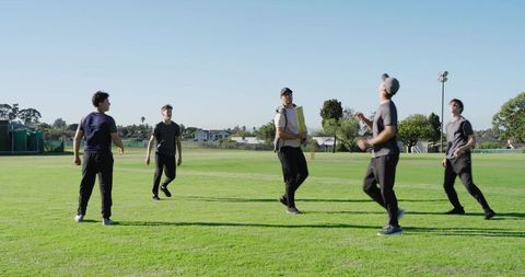 Coach tossing ball while teenagers practicing catching and diving in cricket training