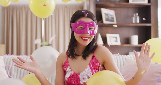 Woman in a bright sequin dress and pink mask enjoying an indoor party surrounded by balloons and confetti. Ideal for festive events, celebrations, and party invitations or advertisements.