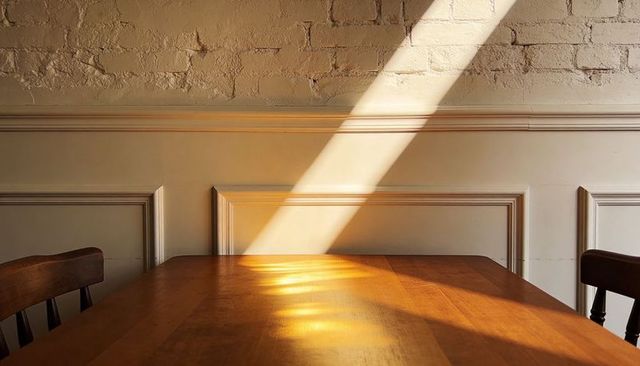 Sunbeam crossing wooden dining table with brick wall and classic wall paneling, warm glow