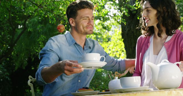 Couple sharing a joyful moment while drinking tea in a serene garden setting under warm sunlight. Ideal for illustrating concepts like togetherness, leisure activities, outdoor living, moments of happiness, and relaxation. Great for use in lifestyle blogs, advertisements promoting outdoor furniture, and articles on relationship tips.