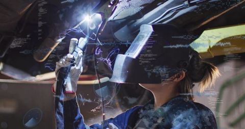 Female welder repairing car undercarriage on lift wearing welding helmet and gloves